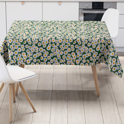 Rechteckige Wachstuch-Tischdecke mit dichtem Gänseblümchen-Muster. Zahlreiche weiße Blüten mit gelber Mitte bedecken einen grünen Hintergrund aus Blättern und Gräsern und erzeugen die Optik einer blühenden Sommerwiese. Zwischen den Blüten sind vereinzelt kleine Marienkäfer zu sehen, die dem floralen Design einen natürlichen und verspielten Akzent verleihen. Die Tischdecke fällt über die Kanten eines Tisches herab.