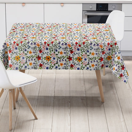 Weiße Wachstuch-Tischdecke mit dichtem, farbenfrohem Wildblumenmuster. Rote, gelbe, orangefarbene, blaue und violette Blüten sowie grüne Blätter und Ranken verteilen sich gleichmäßig über die gesamte Oberfläche und erinnern an eine blühende Sommerwiese im Landhausstil. Die rechteckige Tischdecke ist dekorativ über einen Tisch drapiert.