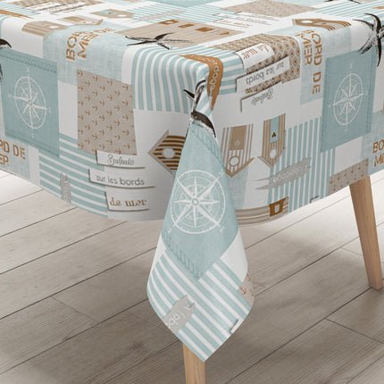 Maritime Wachstuch-Tischdecke mit Patchwork-Muster in Türkis, Beige und Weiß, verziert mit Strandhäusern, Seesternen, Kompassrosen, Streifen und dekorativen Schriftzügen im Küstenstil.