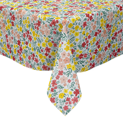 Bunte Wachstuch-Tischdecke mit dichtem Streublumenmuster in Rot, Gelb und Rosa sowie grünen Blättern auf hellem Hintergrund, über eine rechteckige Tischkante drapiert.