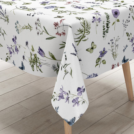 Weiße Wachstuch-Tischdecke mit zartem Wiesenblumen-Muster aus Wildblumen, Gräsern, Schmetterlingen und Libellen in sanften Violett-, Blau- und Grüntönen.