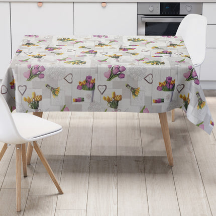 Wachstuch-Tischdecke mit romantischem Patchwork-Dessin in Hellgrau, Weiß und Creme. Das Muster zeigt rosa, violette und gelbe Tulpensträuße, Herzmotive, Spitzenornamente und Holzoptik-Elemente in harmonischer Anordnung. Die floralen Motive verleihen der Tischdecke einen frühlingshaften Landhausstil und schaffen eine freundliche, gemütliche Atmosphäre.